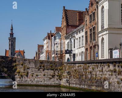 Rangée de bâtiments historiques en briques le long d'un canal avec une tour d'église en arrière-plan sous un ciel bleu, vieilles maisons historiques avec des tours d'église et Banque D'Images