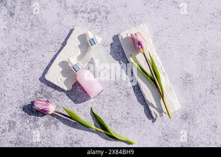 Deux flacons compte-gouttes mats avec un produit naturel pour les soins quotidiens de la peau du visage sur un fond de marbre avec des tulipes. Concept de soin et de beauté Banque D'Images