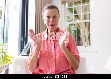 Une femme caucasienne âgée aux cheveux gris courts tapant des mains à la maison, en appel vidéo Banque D'Images