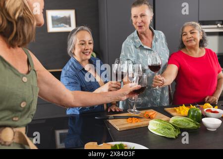 Diverses amies seniors appréciant le vin à la maison dans la cuisine Banque D'Images