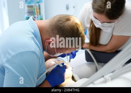 Dentiste avec assistant sous microscope traite les dents du patient. La dentisterie moderne progressive. Nettoyage professionnel des dents Banque D'Images