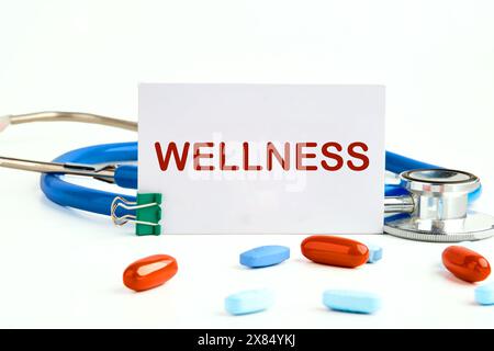 Wellness - concept de mot écrit sur une carte de visite à côté d'un stéthoscope avec des pilules, des vitamines Banque D'Images