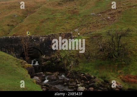 Une structure de pont construite en pierre avec un ruisseau naturel coulant en dessous, sur le flanc d'une montagne. 27 avril 2024. Une vue depuis les Black Mountains dans le Carmarthenshire, au sud du pays de Galles. Photos prises un matin de bruine fine constante avec une mauvaise visibilité. Banque D'Images