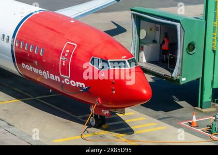 Un boeing 737-800 de Norwegian Airlines, dans une livrée rouge et blanche typique, sur le point d'accoster à une porte d'embarquement. Soleil brillant, couleurs vives Banque D'Images