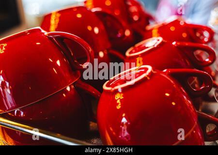 Un tas de tasses en céramique rouge propres pour le thé ou le café sur une étagère de vaisselle dans un café. Foyer sélectionné. Photo de haute qualité Banque D'Images