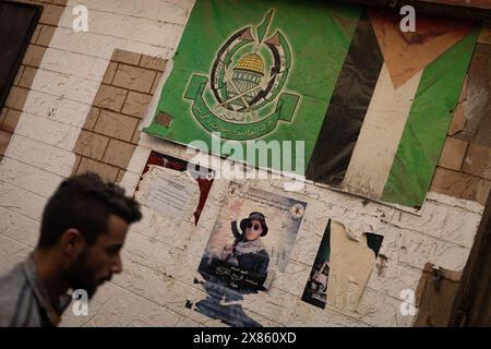 Beyrouth, Liban. 18 mai 2024. Un homme marche devant des affiches représentant l’emblème du Hamas, un drapeau palestinien, et a tué le combattant palestinien du Jihad islamique (JIP) Mohammad Friej dans le camp de réfugiés de Bourj el-Brajneh, Beyrouth, Liban, le 18 mai 2024. Environ 25 000 Palestiniens vivent à Bourj el-Brajneh. (Photo de Collin Mayfield/Sipa USA) crédit : Sipa USA/Alamy Live News Banque D'Images