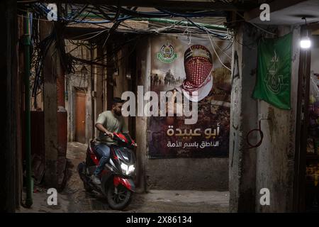 Beyrouth, Liban. 18 mai 2024. Un homme conduit une moto près d'une affiche du porte-parole du Hamas Abu Obaida dans le camp de réfugiés de Bourj el-Brajneh, Beyrouth, Liban, le 18 mai 2024. Environ 25 000 Palestiniens vivent à Bourj el-Brajneh. (Photo de Collin Mayfield/Sipa USA) crédit : Sipa USA/Alamy Live News Banque D'Images