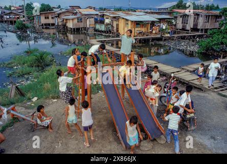Philippines, Mindanao, enfants sur toboggan dans un bidonville inondé de Davao. Banque D'Images
