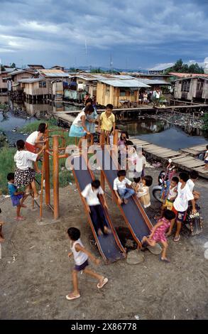 Philippines, Mindanao, enfants sur toboggan dans un bidonville inondé de Davao. Banque D'Images