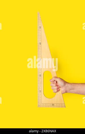 Main d'homme tenant une règle triangulaire en bois sur un fond jaune avec espace de copie Banque D'Images