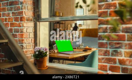 Ordinateur portable avec écran vert maquette affichage debout sur une table dans le salon élégant. Vue de l'extérieur de la fenêtre d'un bâtiment à plusieurs étages en brownstone de style Brooklyn. Concept de travail à domicile. Banque D'Images