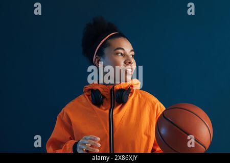 Portrait d'une joueuse professionnelle de basket-ball regardant loin dans un studio. Joueuse de basket-ball confiante portant des vêtements de sport orange. Banque D'Images