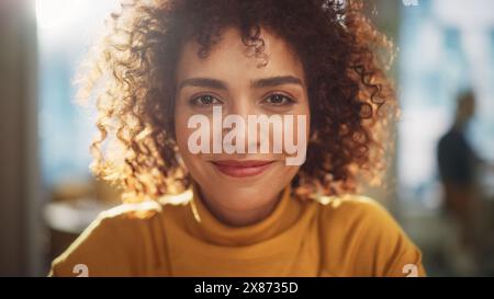 Gros plan Portrait d'une jeune femme du moyen-Orient aux cheveux bouclés courts, à la recherche d'un appareil photo, portant un pull jaune. Belle femme multiethnique diversifiée portant jaune souriant et étant heureuse. Banque D'Images