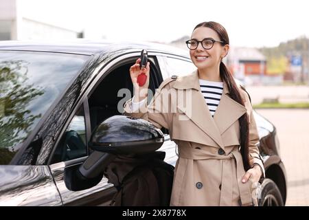 Femme tenant la clé à bascule de voiture près de son véhicule à l'extérieur Banque D'Images