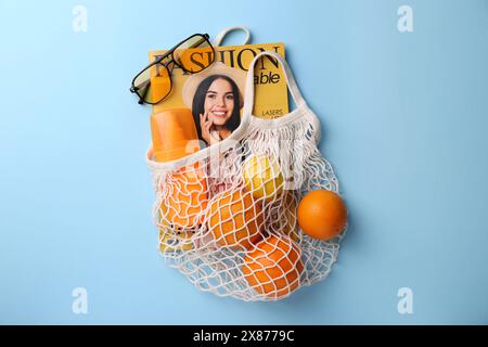 Sac à ficelle avec magazine, fruits et accessoires d'été sur fond bleu clair, pose plate Banque D'Images