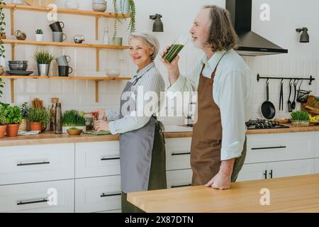 Homme buvant de la jucie d'herbe de blé debout avec une femme dans la cuisine à la maison Banque D'Images