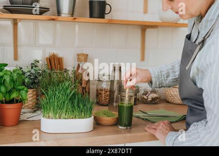 Femme mélangeant du jus d'herbe de blé dans un verre à la maison Banque D'Images