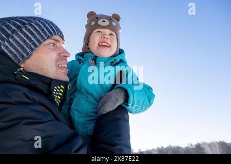 Homme souriant portant son fils en hiver sous le ciel Banque D'Images