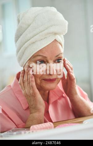 Femme âgée souriante s'appliquant sous les patchs oculaires à la maison Banque D'Images