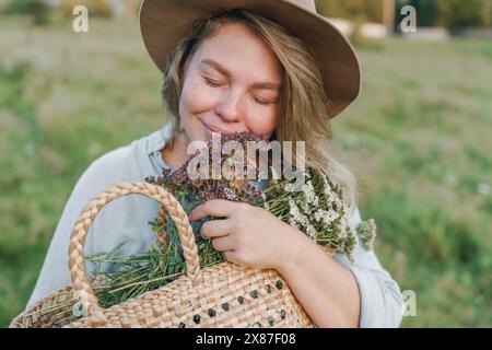 Femme souriante avec les yeux fermés embrassant le panier de fleurs Banque D'Images