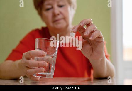 Femme âgée tenant verre d'eau et pilule à la maison Banque D'Images