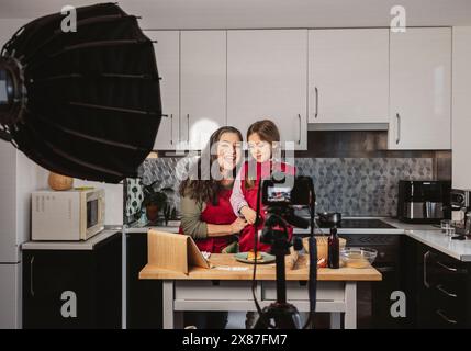 Heureuse grand-mère vlogging avec petite-fille dans la cuisine à la maison Banque D'Images