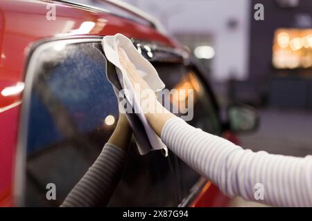 Femme essuyant la voiture avec la serviette après lavage au garage Banque D'Images