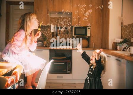 Frères et sœurs jouant avec la bulle de savon dans la cuisine à la maison Banque D'Images