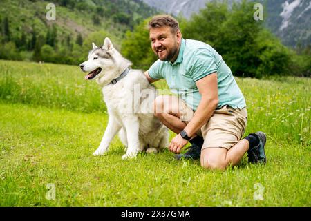 Homme mûr par chien Husky agenouillé sur l'herbe Banque D'Images