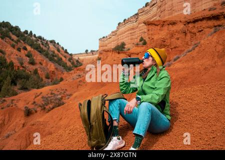 Femme fatiguée buvant de l'eau assise avec sac à dos canyon rouge prenant pause Banque D'Images