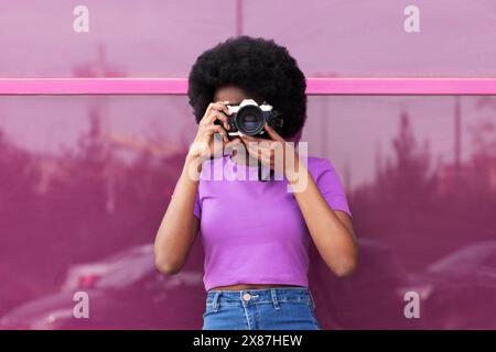 Jeune femme photographiant à travers la caméra devant la fenêtre magenta Banque D'Images