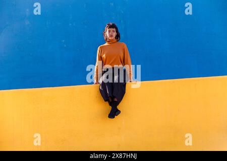 Jeune femme assise sur un mur jaune Banque D'Images