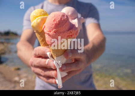 Homme tenant de la crème glacée colorée dans des tasses de gaufres le jour ensoleillé au bord de la mer Banque D'Images