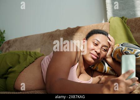 Femme enceinte prenant selfie par téléphone portable tout en étant allongé sur le canapé à la maison Banque D'Images