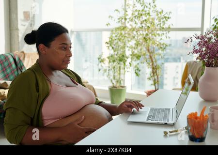 Mère enceinte utilisant un ordinateur portable assis à table Banque D'Images