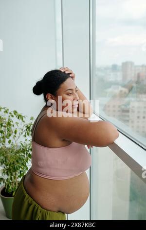 Femme enceinte réfléchie regardant par la fenêtre à la maison Banque D'Images