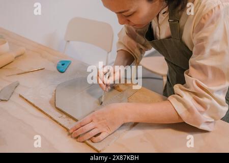 Artisan qualifié coupant l'argile sur la table au lieu de travail de poterie Banque D'Images