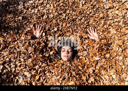 Jeune femme insouciante couvrant le corps avec des feuilles d'automne Banque D'Images