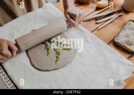 Mains de femme imprimant des fleurs sur de l'argile avec rouleau à pâtisserie à la maison Banque D'Images