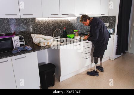 Homme âgé handicapé avec des jambes prothétiques cuisinant dans la cuisine à la maison Banque D'Images