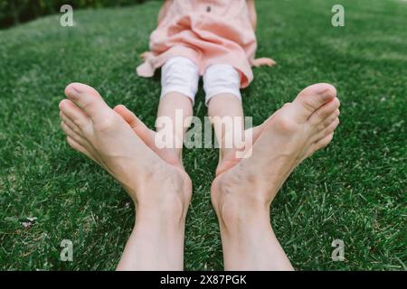 Mère joignant les pieds avec sa fille assise sur l'herbe au parc Banque D'Images