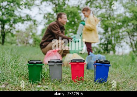 Poubelles à jouets multicolores avec père et fille collectant des bouteilles en plastique dans la forêt Banque D'Images