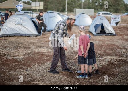 23 mai 2024, Israël, Kibboutz ami'ad : les Israéliens évacués des zones nord près de la frontière libanaise en raison des tensions transfrontalières continues, se tiennent debout au milieu de tentes lors d'un rassemblement appelant le gouvernement à les laisser rentrer chez eux. Photo : Ilia Yefimovich/dpa Banque D'Images