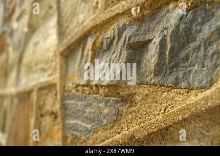 Vue rapprochée détaillée d'un mur de pierre avec des grains de sable en couches sur sa surface, mettant en évidence la texture et l'abstraction des éléments. Banque D'Images