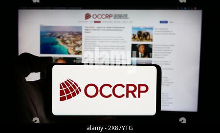 Personne tenant un téléphone cellulaire avec le logo du projet de signalement du crime organisé et de la corruption (OCCRP) devant la page Web. Concentrez-vous sur l'affichage du téléphone. Banque D'Images