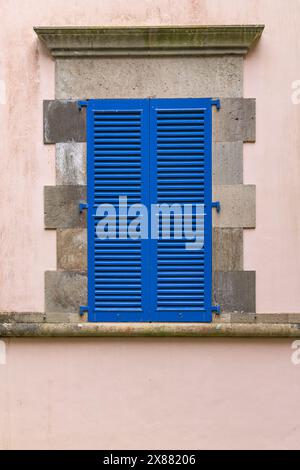 Furnas, Sao Miguel, Açores, Portugal. Fenêtre bleue à volets sur un bâtiment en stuc rose. Banque D'Images