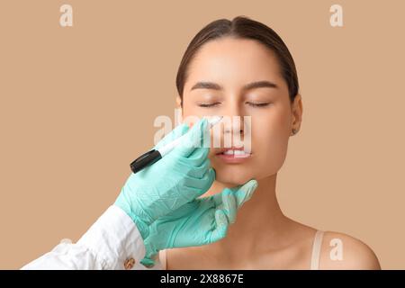 Docteur en gants de protection dessinant des marques sur le nez de la femme pour la chirurgie plastique sur fond beige Banque D'Images