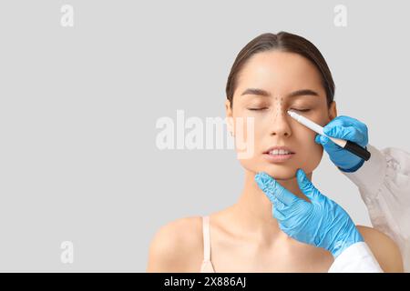 Docteur en gants de protection dessinant des marques sur le nez de la femme pour la chirurgie plastique sur fond blanc Banque D'Images