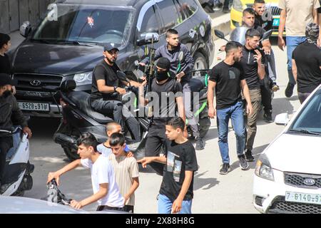 Jénine, Palestine. 23 mai 2024. Des hommes armés défilent alors que les personnes en deuil portent les corps de Palestiniens, certains drapés dans les drapeaux du groupe militant du Jihad islamique lors de leurs funérailles dans la ville de Djénine, en Cisjordanie. L’armée israélienne a déclaré avoir achevé une opération de deux jours en Cisjordanie occupée qui a tué et blessé plusieurs Palestiniens, selon le ministère palestinien de la santé. Le groupe militant palestinien Jihad islamique a déclaré que ses combattants ont combattu les forces israéliennes. Crédit : SOPA images Limited/Alamy Live News Banque D'Images