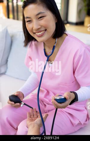 Une infirmière asiatique et un patient d'âge moyen vérifient la pression artérielle à domicile Banque D'Images